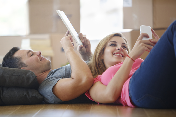 Young couple using mobile phone and tablet in new home